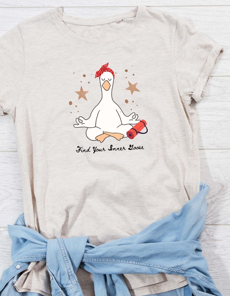 May include: Beige t-shirt with a cartoon goose meditating, wearing a red headband and with a yoga mat. The text "Find Your Inner Goose" is printed below. Brown star and dot accents surround the goose.