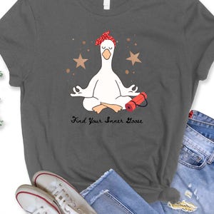 May include: Dark grey t-shirt with a cartoon goose in a yoga pose, wearing a red bandana. The design includes two brown stars and the text "Find Your Inner Goose". A red yoga mat is next to the goose.