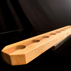 May include: A wooden shot glass holder with eight round holes. The holder is made of light brown wood with a darker brown wood accent.