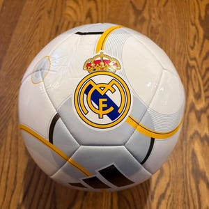 Puede incluir: Un juego de tres tazas de cer&aacute;mica con un esmalte moteado de color crema. Cada taza presenta un dise&ntilde;o pintado a mano diferente: una hoja azul y verde, una flor amarilla y una baya roja. Las tazas tienen una forma simple y redondeada.