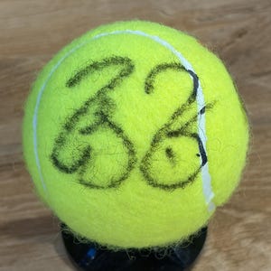 May include: A white ceramic mug with a black handle and the text "But First, Coffee" in a black, handwritten-style font. The mug is on a white surface.