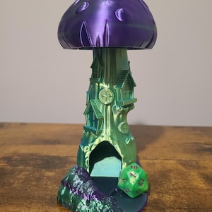 May include: A 3D printed mushroom house with a green and purple iridescent finish. The house has a small opening at the base and a green dice is sitting in front of the opening.