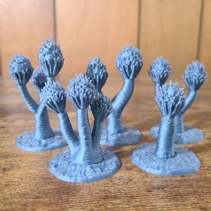 May include: A set of seven blue 3D printed miniature trees with a unique branching design. The trees are all different heights and have a textured surface.