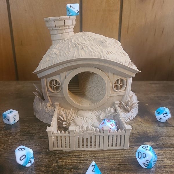 May include: A 3D printed miniature house with a thatched roof and a fence, designed to hold dice. The house has a round opening in the front and a chimney on the roof. There are several blue and white dice scattered around the house.