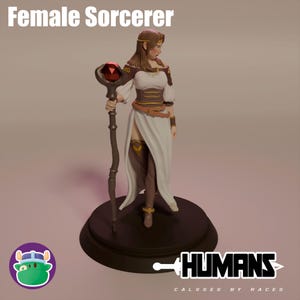 Könnte beinhalten: Eine weibliche Zauberer-Miniaturfigur mit einem Stab und einem roten Edelstein. Die Figur trägt ein weißes Kleid mit braunen Akzenten und einem goldenen Gürtel. Die Figur steht auf einem schwarzen Sockel mit dem Wort "HUMAINS" darauf.