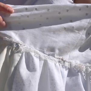 K&ouml;nnte beinhalten: Ein wei&szlig;es Kleid mit einer Spitzenborte und einem Sternenmuster. Das Kleid ist aus einem weichen, leichten Stoff.