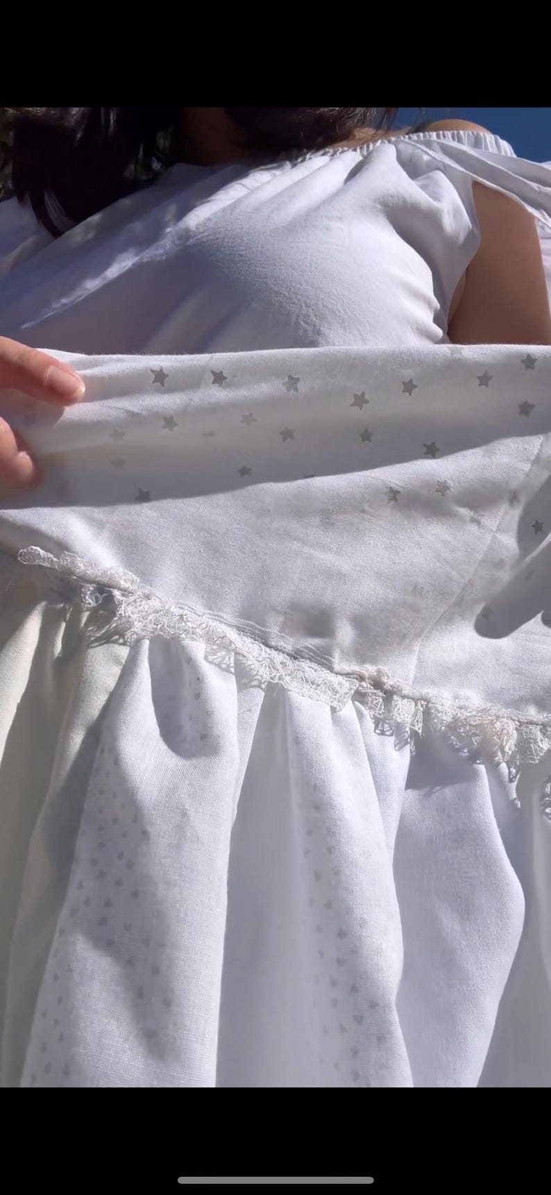 K&ouml;nnte beinhalten: Ein wei&szlig;es Kleid mit einer Spitzenborte und einem Sternenmuster. Das Kleid ist aus einem weichen, leichten Stoff.