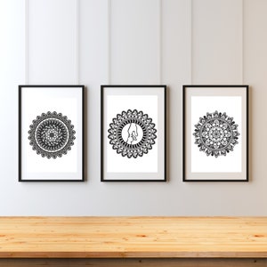May include: Three framed black and white mandala art prints. Each print features a unique, intricate circular design. The frames are black, and the background is white. The prints are displayed on a light wood surface against a white wall.