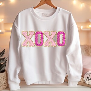May include: White sweatshirt with a pink and gold glitter XOXO design.