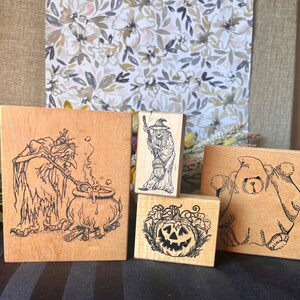 Op de afbeelding: Vier houten stempels met Halloween-thema's. De stempels tonen een heks die een ketel roert, een heks die op een bezem rijdt, een uitgeholde pompoen en een spook.