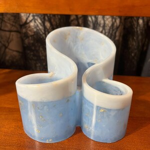 May include: A blue and white resin desk organizer with a unique, flowing design. The organizer features three compartments and is accented with gold flecks. The top and rims are white, while the base is a light blue color.