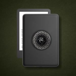 May include: A black e-reader device featuring a circular grip attachment on the back. The attachment displays a white line-art illustration of an anatomical heart surrounded by a decorative, ornate circular border with star-like accents.