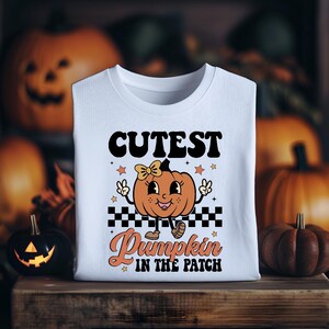 May include: White t-shirt with a cute cartoon pumpkin wearing a bow and the text "Cutest Pumpkin in the Patch".