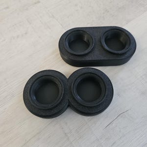Pode incluir: Dois porta-velas circulares de plástico preto com uma borda elevada. Os porta-velas estão conectados um ao outro.