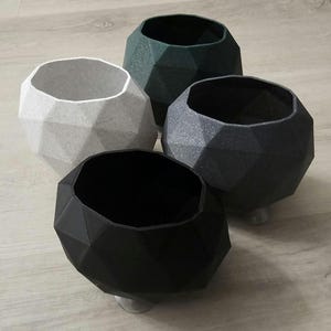 May include: Four geometric planters in different colours: white, black, dark green, and grey. The planters are made of a textured material and have a unique, faceted design.