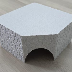 Könnte beinhalten: Eine weiße, strukturierte, steinartige Struktur mit einem abgerundeten Torbogen. Die Struktur besteht aus einem leichten Material und hat eine raue, strukturierte Oberfläche.