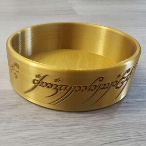 Pode incluir: Uma tigela dourada com a inscrição "Um Anel para governá-los a todos, Um Anel para encontrá-los, Um Anel para trazê-los a todos e nas trevas prendê-los" ao redor da borda.