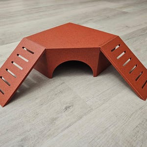 May include: A red wooden hideaway for small pets, featuring two ramps with cut-out steps leading up to the entrance.