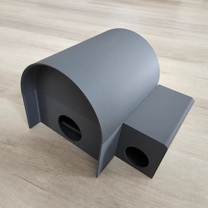Peut inclure: Une maison pour chat de couleur grise, en forme de tunnel incurvé avec deux entrées. La maison est en plastique et a une surface lisse.