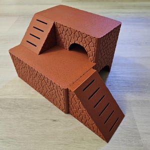 Peut inclure: Une maison de jeu en carton marron à plusieurs niveaux pour petits animaux, avec deux rampes à marches découpées et une entrée en tunnel.