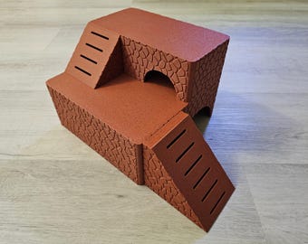 Puede incluir: Una casa de juegos de cartón marrón de varios niveles para animales pequeños, con dos rampas con escalones recortados y una entrada de túnel.