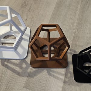 Könnte beinhalten: Drei geometrische Formen, jede in einer anderen Farbe. Die erste ist weiß, die zweite braun und die dritte schwarz. Jede Form ist ein dreidimensionales geometrisches Design mit einer hohlen Mitte.