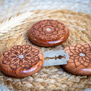 May include: Three wooden discs with intricate laser-etched designs, each with a small metal dot in the centre. A silver razor blade is placed between two of the discs.