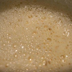 May include: Close-up of a light brown liquid with small bubbles on the surface.