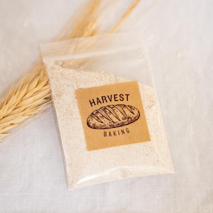 Peut inclure: Un sac en plastique transparent rempli de farine blanche avec une étiquette brune sur laquelle est inscrit "HARVEST BAKING" et un dessin d'une miche de pain.