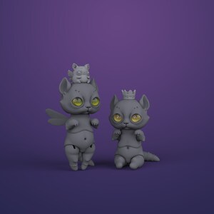 2 gray digital articulated cat dolls in a royal purple studio. Right one with yellow eyes sits and has a crown, left one with green eyes stands and has dragonfly wings and cute chubby winged animal on its head.