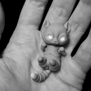 B&W photo of woman holding a tiny 5 cm (2 inch) ball jointed cat with big reflective eyes in her palm.