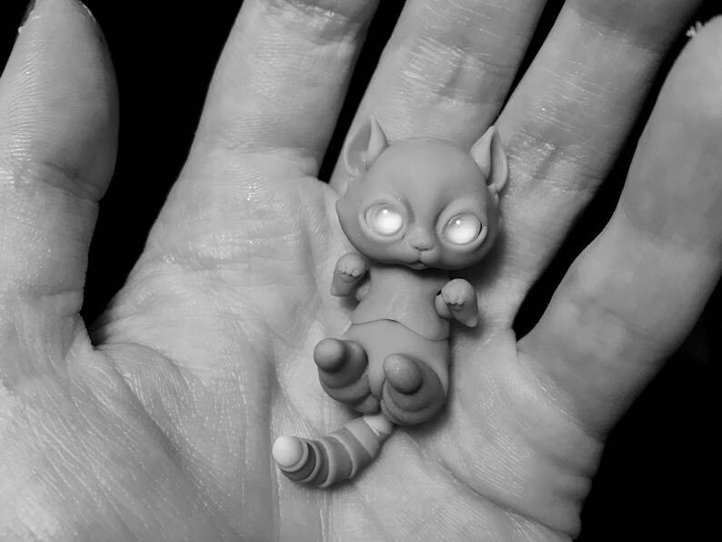 B&W photo of woman holding a tiny 5 cm (2 inch) ball jointed cat with big reflective eyes in her palm.