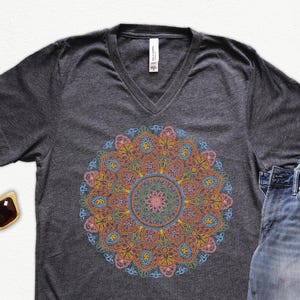 May include: A dark grey V-neck t-shirt with a colorful mandala design printed on the front. The mandala is a circular pattern with intricate details in shades of blue, pink, orange, and yellow.