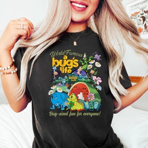 May include: Black t-shirt featuring the text "World Famous a bug's life" with colorful cartoon bugs and flowers. The shirt also has the text "Bug-sized fun for everyone!"