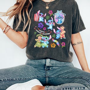Peut inclure: T-shirt gris fonc&eacute; avec un motif color&eacute; de Stitch de Lilo & Stitch, entour&eacute; de fleurs et du texte "Ohana Means Family". Le design comprend diverses images de Stitch dans diff&eacute;rentes poses.