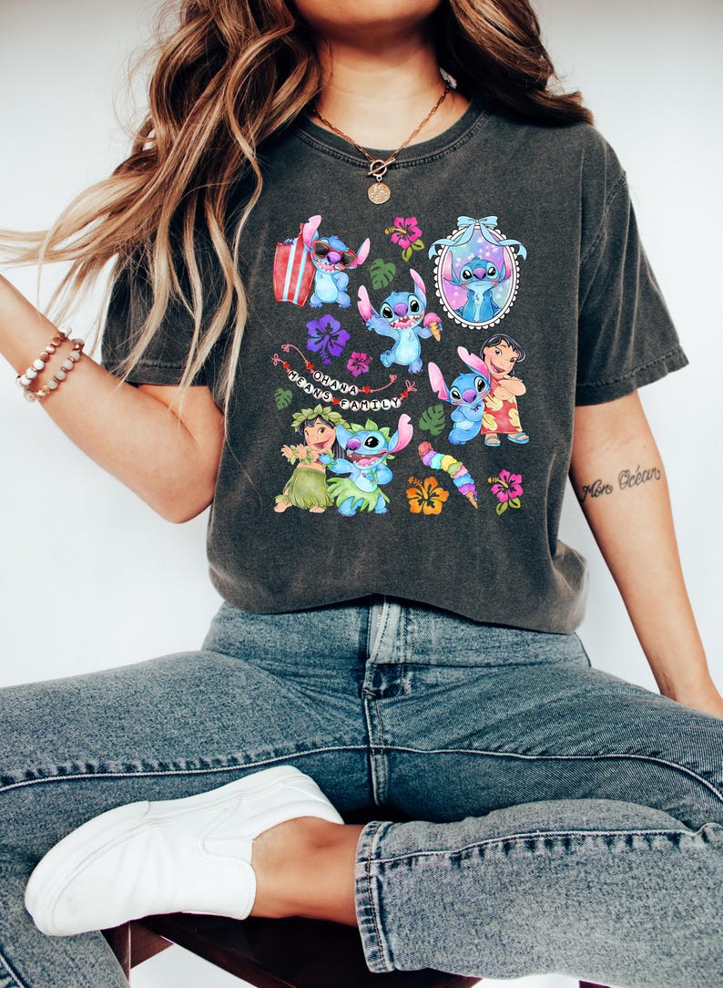 Peut inclure: T-shirt gris fonc&eacute; avec un motif color&eacute; de Stitch de Lilo & Stitch, entour&eacute; de fleurs et du texte "Ohana Means Family". Le design comprend diverses images de Stitch dans diff&eacute;rentes poses.