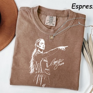 May include: An espresso-colored t-shirt featuring a white graphic print of a basketball player pointing with a signature below. The shirt has a crew neckline and a Comfort Colors brand label at the inner neck. The text Espresso is visible.