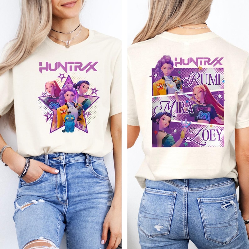 May include: Cream-colored t-shirt featuring a purple star design with the text "HUNTRAX" above a group of animated characters. The back of the shirt displays the names Rumi, Mira, and Zoey, with additional character illustrations.