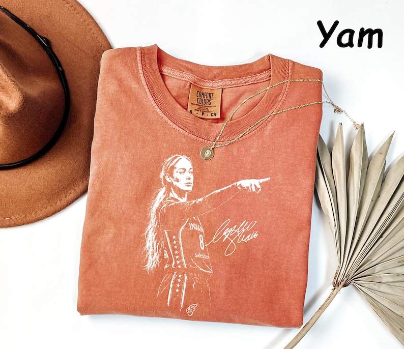 May include: A burnt orange crew neck t-shirt featuring a white graphic print of a basketball player pointing, with the text "Yam" visible in the upper right corner. The shirt has a Comfort Colors brand label at the inner neckline with size S.