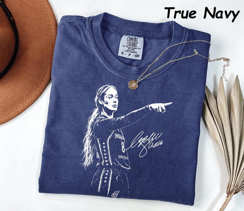 May include: A true navy blue short-sleeve t-shirt featuring a white graphic print of a basketball player pointing forward with a signature. The shirt has a crew neckline and a Comfort Colors brand label on the inside collar showing size small.