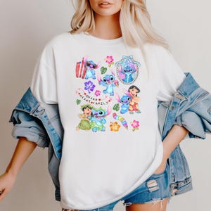 Peut inclure: T-shirt blanc avec un motif color&eacute; de Stitch de Lilo & Stitch, entour&eacute; de fleurs et de l'inscription "Ohana Means Family". Le design pr&eacute;sente Stitch dans diverses poses.