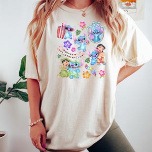 Peut inclure: T-shirt cr&egrave;me avec un motif color&eacute; du personnage Stitch du film Lilo & Stitch. Le motif comprend Stitch dans diverses poses avec des fleurs et le texte "Ohana Means Family".