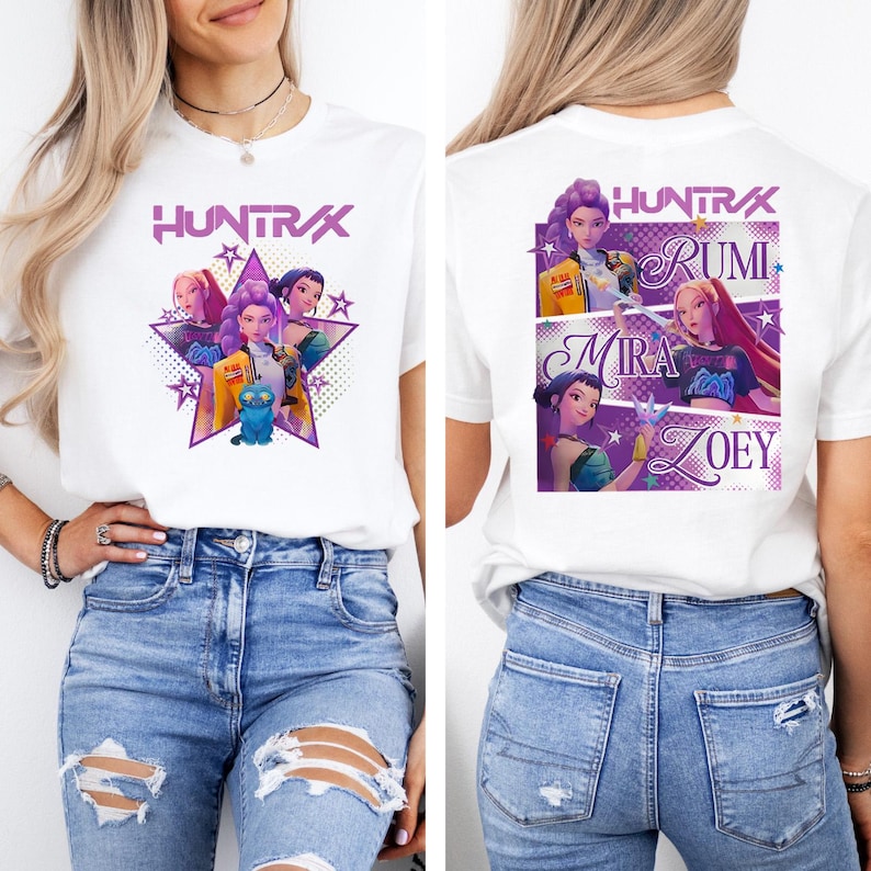 May include: White t-shirt featuring a graphic of a group of animated characters with the text "HUNTRAX" in purple. The front design includes a star shape and a blue creature. The back of the shirt displays the names Rumi, Mira, and Zoey.