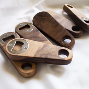 May include: A set of five wooden bottle openers with a metal bottle opener insert. The bottle openers are made of dark wood and have a rounded shape.