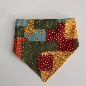 May include: A triangular pet bandana featuring a patchwork design of various fabric squares. The pattern includes olive green with white dots, red with white dots, light blue with a checkered pattern, and yellow with white daisy-like flowers.