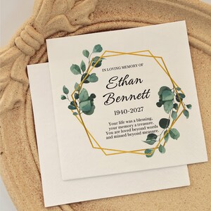 May include: A square white memorial card featuring a gold geometric frame, green eucalyptus leaves, and black text reading: IN LOVING MEMORY OF Ethan Bennett 1940-2027 Your life was a blessing, your memory a treasure, You are loved beyond words and missed beyond measure.