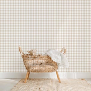 May include: A wicker basket with a white blanket and a teddy bear inside, sitting on a beige rug in front of a wall with a brown and white gingham pattern.