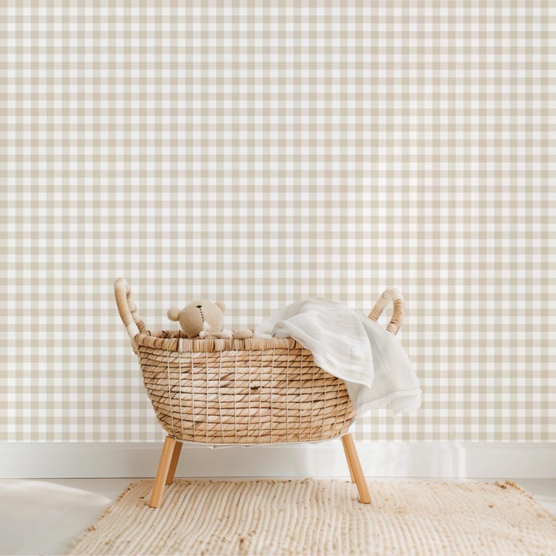 May include: A wicker basket with a white blanket and a teddy bear inside, sitting on a beige rug in front of a wall with a brown and white gingham pattern.