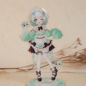 May include: An acrylic standee featuring an anime-style character with short mint green hair, wearing a ruffled mint and brown outfit with a white apron. The character is accompanied by two small cat-like spirits and stands on a round mint base.