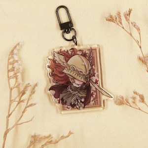 Könnte beinhalten: Ein klarer Acryl-Schlüsselanhänger mit einer Cartoon-Illustration einer Figur mit goldenem Helm, rotem Haar und Schwert. Der Schlüsselanhänger hat einen schwarzen Metallverschluss und einen dekorativen floralen Hintergrund.